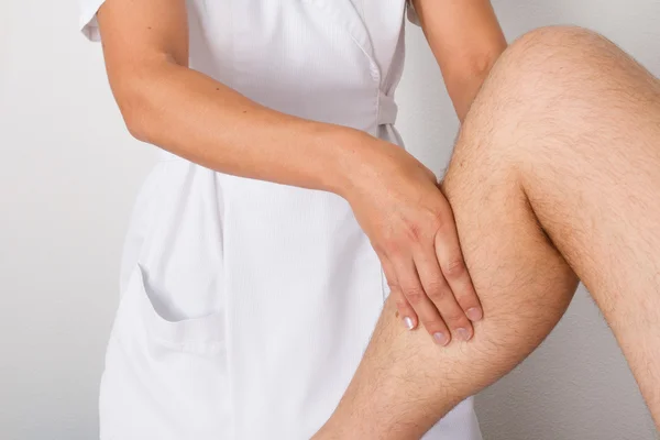 Fisioterapeuta femenina masajeando la pierna de un paciente masculino en una sala de fisioterapia . — Foto de Stock