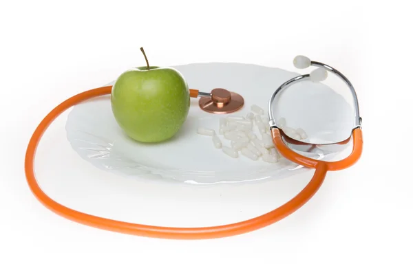 Piller och apple på en tallrik omgiven med stetoskop — Stockfoto