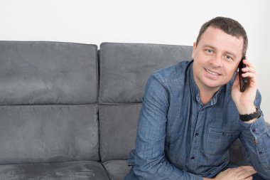 Kanepede bir telefon konuşma yaparken gülümseyen adam