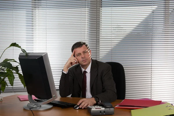 Knappe zakenman werkt met de computer in kantoor is kijken naar de camera. — Stockfoto