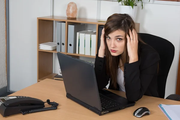 Donna d'affari stanca seduta al tavolo su sfondo grigio. Guardando sul computer portatile — Foto Stock