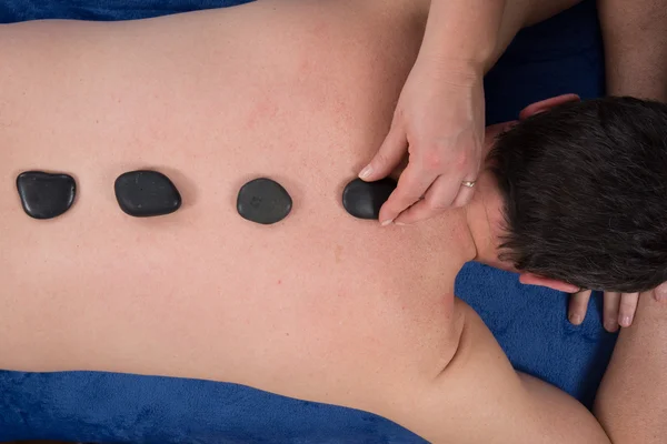 Un hombre en un spa recibiendo un masaje de piedra caliente. plano de estudio . —  Fotos de Stock