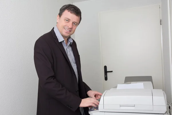 Homem de negócios feliz sorrindo perto de uma máquina de cópia no trabalho — Fotografia de Stock