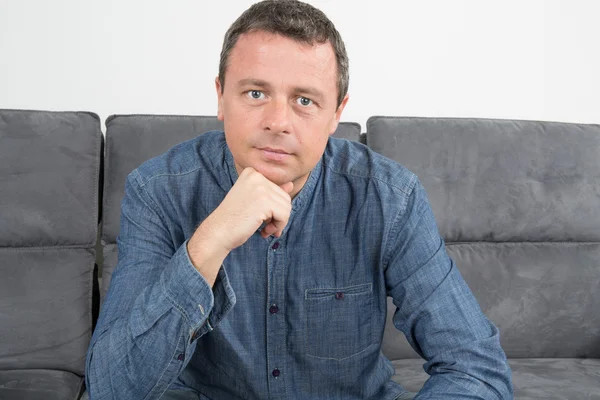 Confident man relaxing at home on the sofa looking at the camera with a friendly smile — Stock Photo, Image