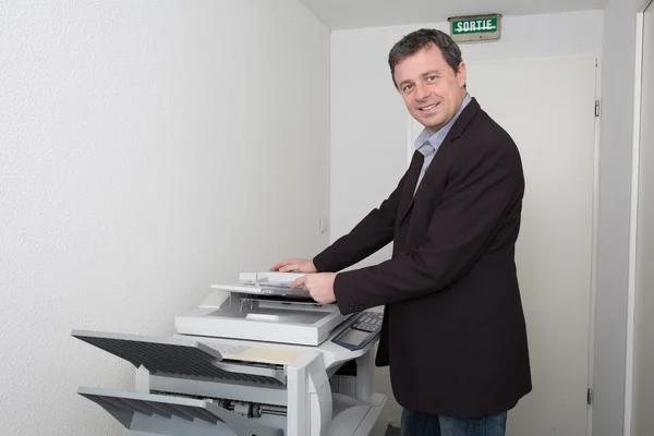 Glücklicher Arbeiter benutzt im Büro ein Kopiergerät — Stockfoto