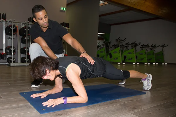 Senior Kvinna utövar assisteras av personlig instruktör på gymmet. Sjukgymnast som hjälper äldre kvinna i hennes träning på health club. — Stockfoto