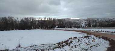 Bulutlu bir günde, gün batımında kar kalıntılarıyla dağlık bir manzara.