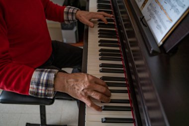 Evde piyano çalan yaşlı bir beyefendinin elleri ve kolları.