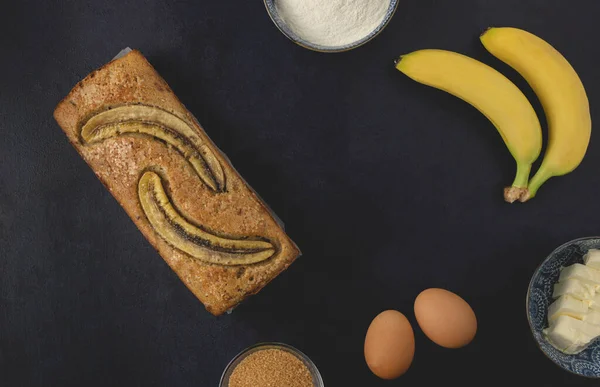 Homemade banana nut bread loaf isolated on the dark background. Banana bread ingredients. Top view, flat lay.
