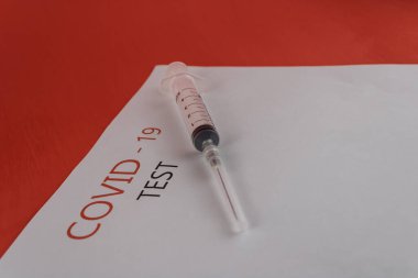 Metni olan beyaz sayfa: covid 19 testi ve kırmızı zemin üzerinde yakın plan bir şırınga