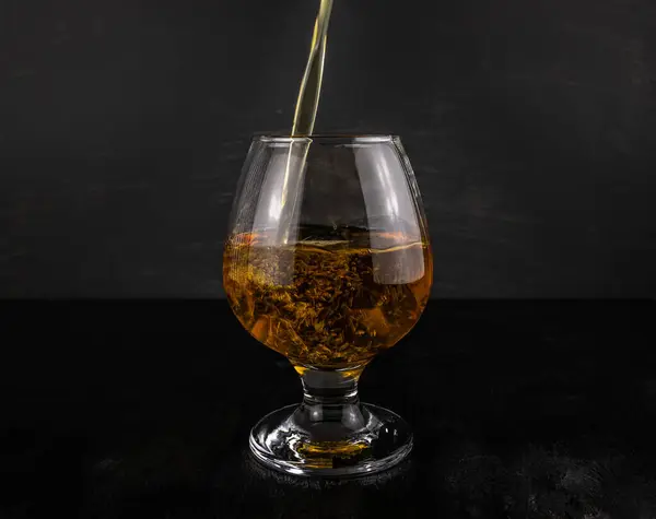 Glas Met Gietende Cognac Close Een Donkere Houten Ondergrond — Stockfoto