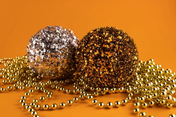 Golden and silver ball with glitter and Christmas beads on an orange background.