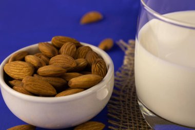 Badem ve bir bardak taze süt mavi arka planda yakın plan..