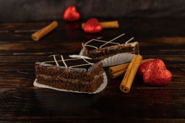 Çikolata kremalı iki kek, tarçın ve siyah ahşap arka planda kalpler..