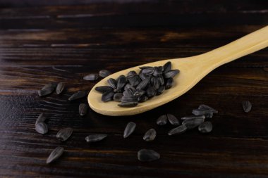 Tohumlar koyu bir arka planda açık renkli tahta bir kaşığa saçılmış.