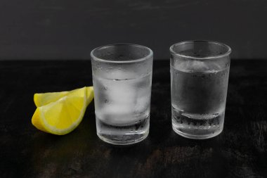 İki buzlu bardak votka ve koyu ahşap arka planda bir limon.