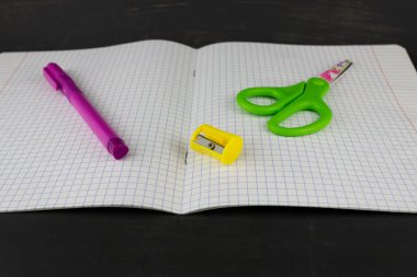 Bir defter, kalem, bileyici ve makas yakın planda..