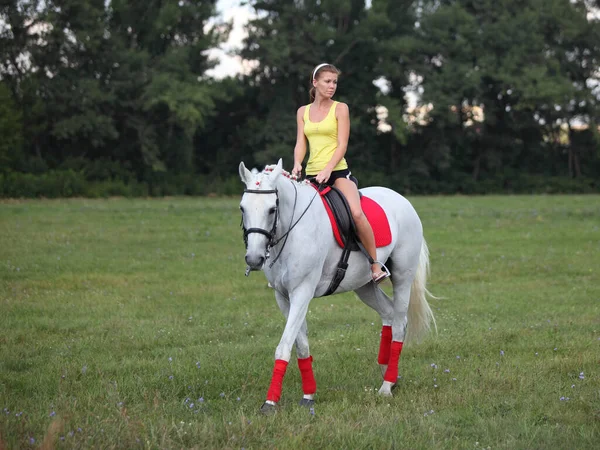 美しいブロンドの女の子は夏の牧草地で乗馬 — ストック写真