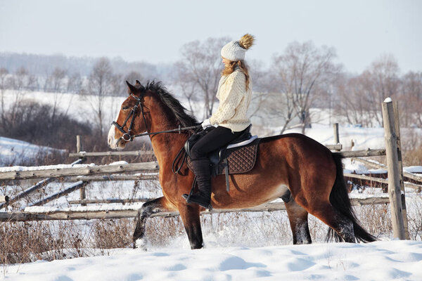 Pretty woman riding her horse through snow country road