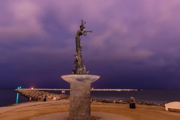 Mermaid statue beacon stands tall over harbor mouth rock jetty as ominious stormy clouds cirlce the sky overhead.