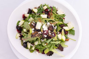 Üstünde kuru erik ve kızarmış ekmek olan büyük bir kâse salata manzarası..