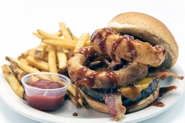 Hamburgerin üzerine barbekü sosu serpiştirilmiş büyük soğan halkaları patates kızartması ve sos ile servis edilir..