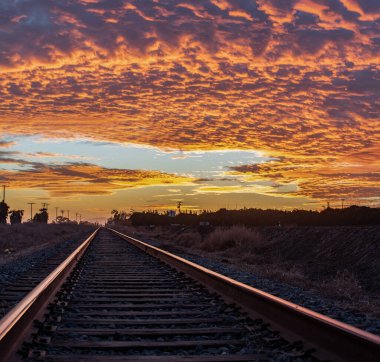 Demiryolunun tren rayları ufkun gökyüzündeki renkli bulutlarla buluştuğu yerde kesişiyor..