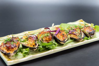 Appetizer of baked mussels drenched in delicious sauce with beautiful presentation on bamboo print plate.