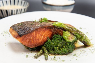 Thick piece of salmon steak over a bed of sauteed vegetables with rice and bowl of miso soup.