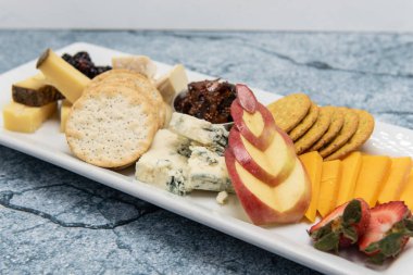 Sunum için oyulmuş elmayla süslenmiş çeşitli peynir, kraker ve meyve tabağı..