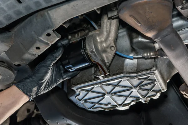 Oil drains from from beneath vehicle as mechanics gloved hand removes filter during routine maintenance fluid change at garage.