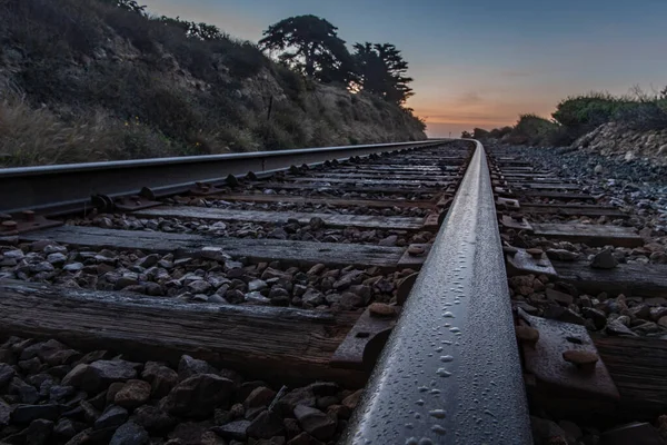 Drops of dew from the morning moisture wets the surface of the track track rail leading up to the horizon at dawn.