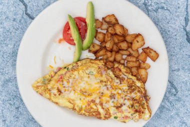 Mükemmel derecede pişirilmiş omlet manzarası katlanmış ve küp patates ve dilimlenmiş avokado ile servis ediliyor..