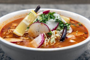 Spicy Pozole stew served loaded with meat and vegetables in a large hearty bowl. clipart