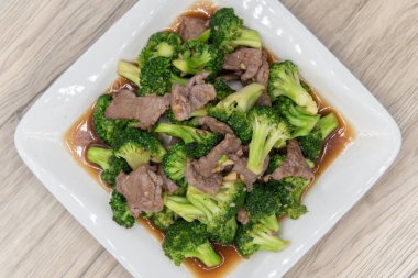 Tabakta et ve sos ile servis edilen büyük bir baharatlı Tayland brokolisi yığını manzarası.