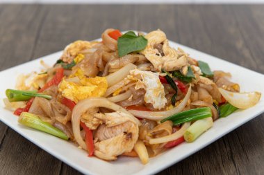 Lezzetli Tayland lezzeti için büyük erişteler fesleğen ve sebze yığınının üstünde kızarır..