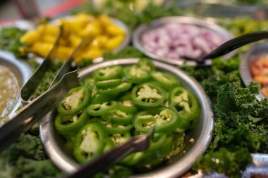 Dilimlenmiş jalapeno biberleri bir çift maşayla servis edilir ve salsa tabağına eklenir..