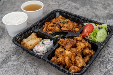 Bento kutusu susamlı tavuk, baharatlı tavuk, salata, gyoza köftesi, pilav ve miso çorbasıyla dolu..