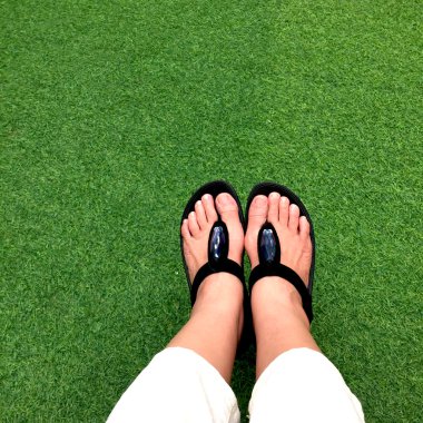 Yeşil yemyeşil suni çim, yaz ve tatil konsepti siyah Flip flop 