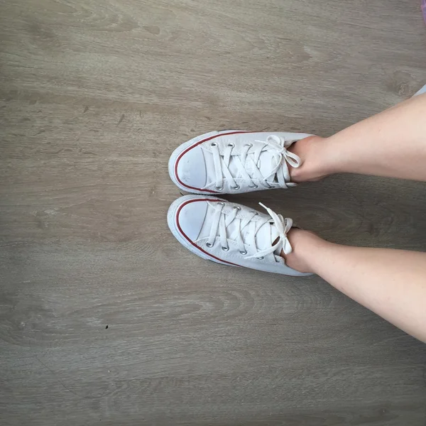 Vita sneakers på flicka ben på trä bakgrund — Stockfoto