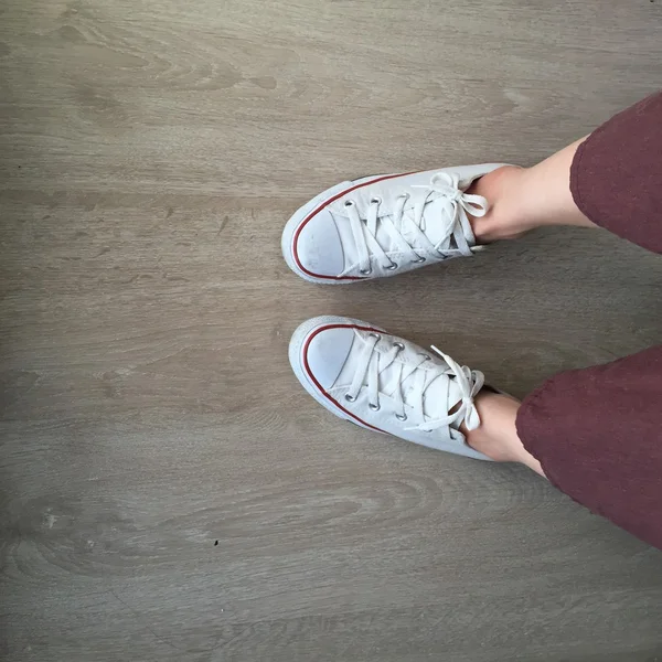 Άσπρα πάνινα παπούτσια στα πόδια κορίτσι σε φόντο ξύλου — Φωτογραφία Αρχείου