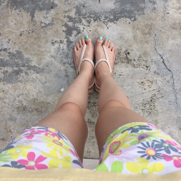 Kvinnliga ben bär flip flop och korta byxor (blomma) på mark eller golv. Topp-vy — Stockfoto