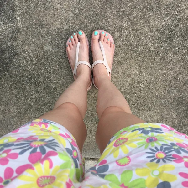 女性の足を着用フリップフロップとショートパンツ (花) 地面や床に.上面図 — ストック写真