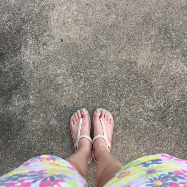 Piernas femeninas con chanclas y pantalones cortos (flor) en tierra o suelo. Vista superior —  Fotos de Stock