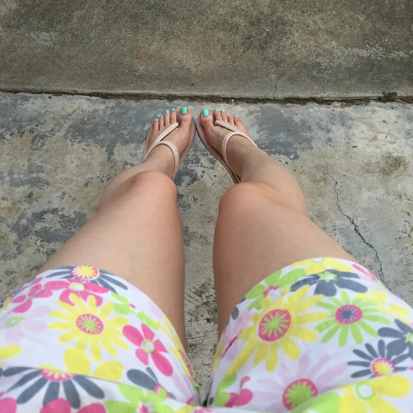 Жіночі ноги носять фліп-флоп і короткі штани (квітка) на землі або підлозі. Вид зверху — стокове фото