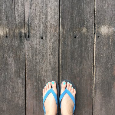 Ahşap üzerinde Flip flop giyen kadın bacaklar. Üst görünüm 