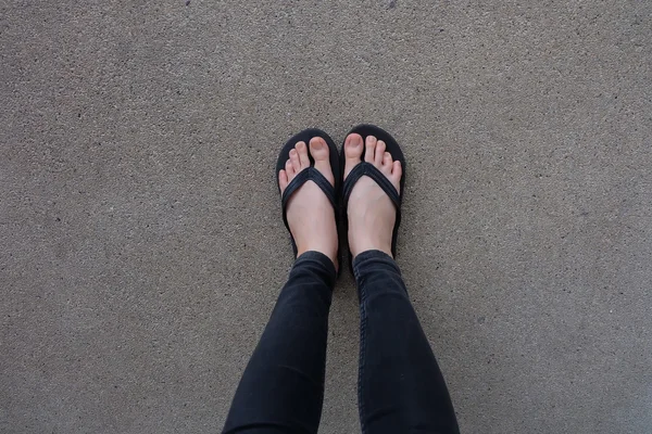 Jong meisje benen in zwarte Flipflop sandalen op vloer of Grunge — Stockfoto