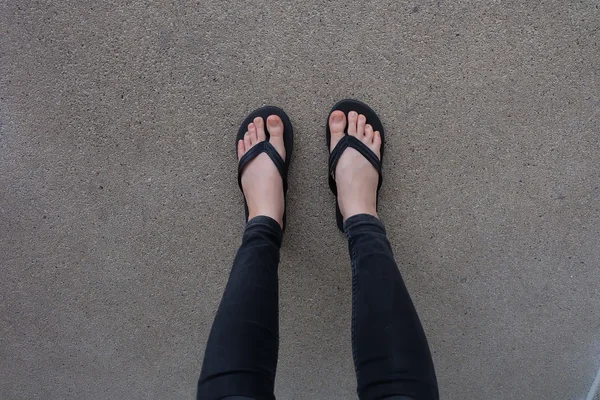 Junge Mädchenbeine in schwarzen Flipflop-Sandalen auf dem Boden oder Grunge — Stockfoto
