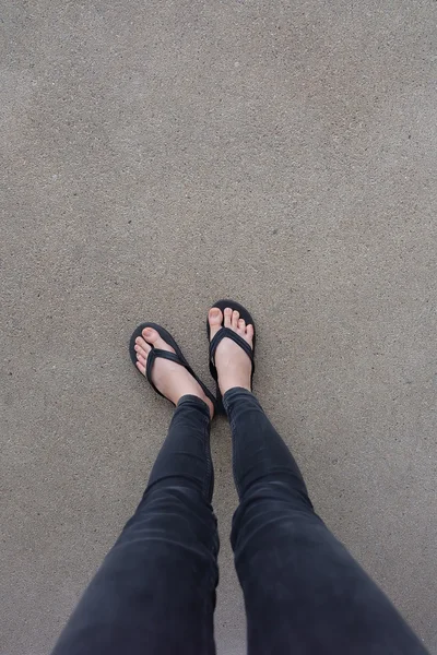 Junge Mädchenbeine in schwarzen Flipflop-Sandalen auf dem Boden oder Grunge — Stockfoto