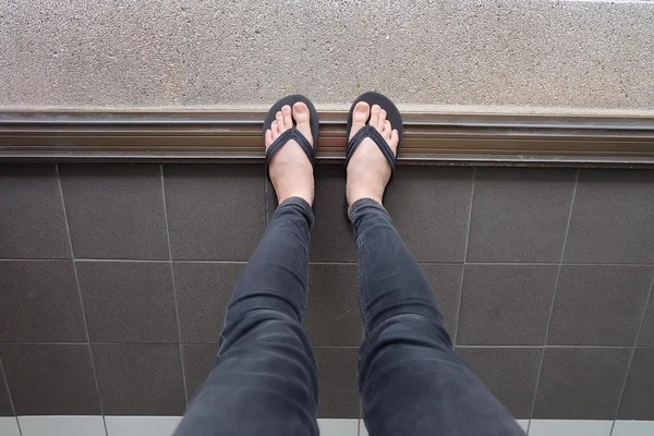 Jong meisje benen in zwarte Flipflop sandalen op vloer of Grunge — Stockfoto